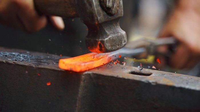 Blacksmith hammering glowing metal on anvil