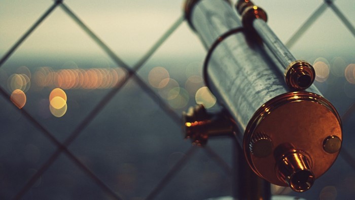 Telescope looking out over city lights through a fence