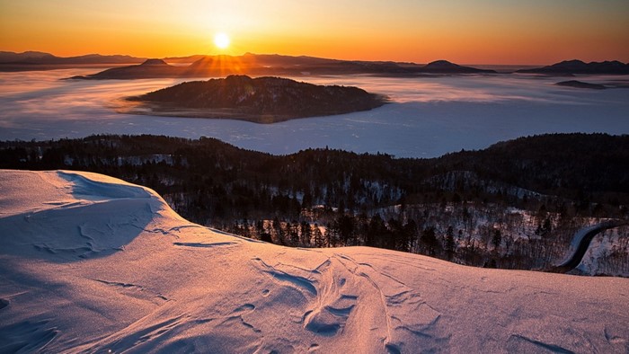 Winter sunrise over a misty valley with snow-covered mountains