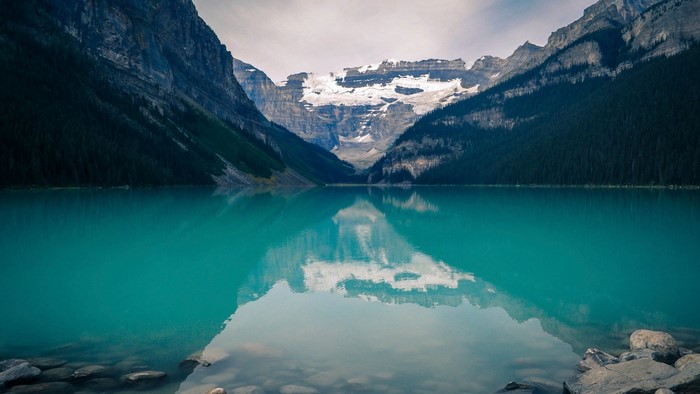 Turquoise lake reflecting snow-capped mountains and pine forest