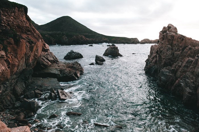Rocky coastline with waves crashing against cliffs and a mountain in the background