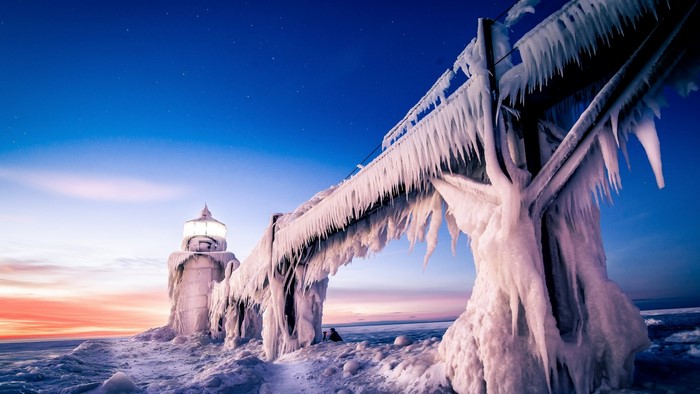 Frozen lighthouse pier in winter at sunset