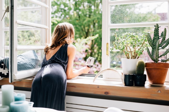 Woman in dark dress holding wine glass by window