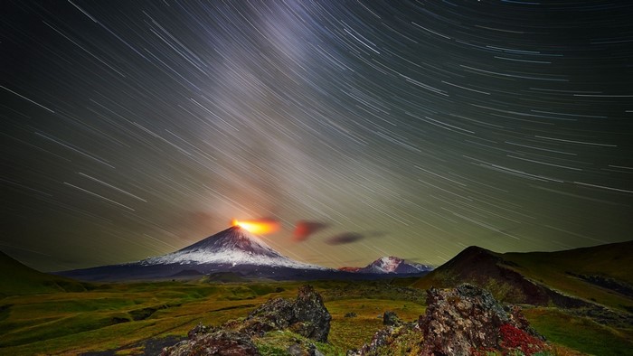 Volcano erupting at night with star trails