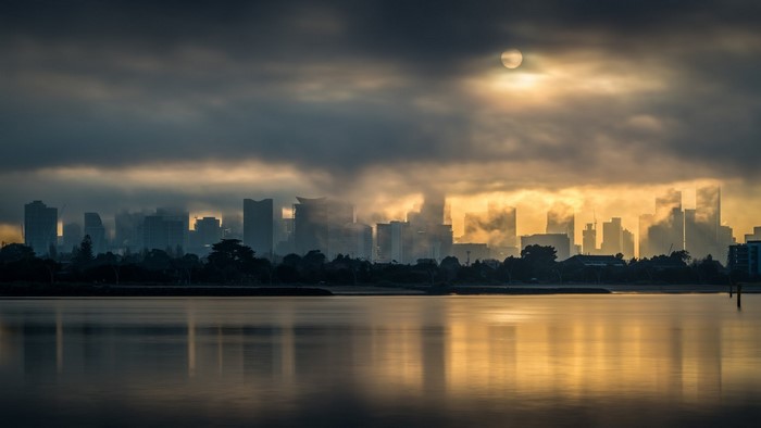City skyline at sunrise with sun and clouds over water