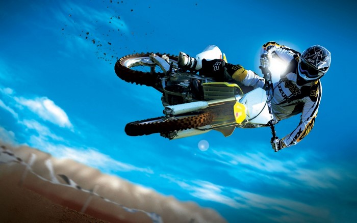 Motocross rider performing a jump against a blue sky