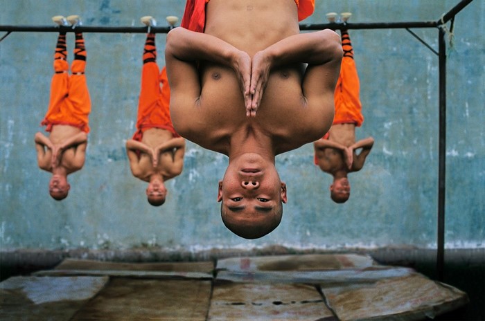 Monks hanging upside down from a bar