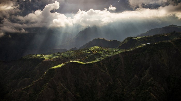 Sun rays breaking through clouds over mountains and fields