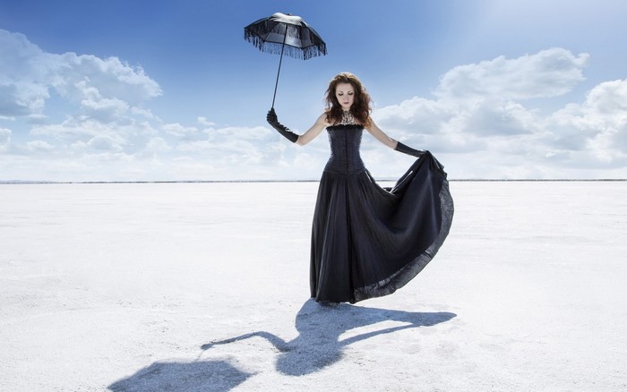 Woman in black dress holding umbrella on salt flats