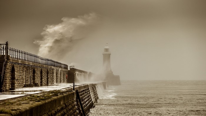 Stormy sea with waves crashing near a lighthouse and pier