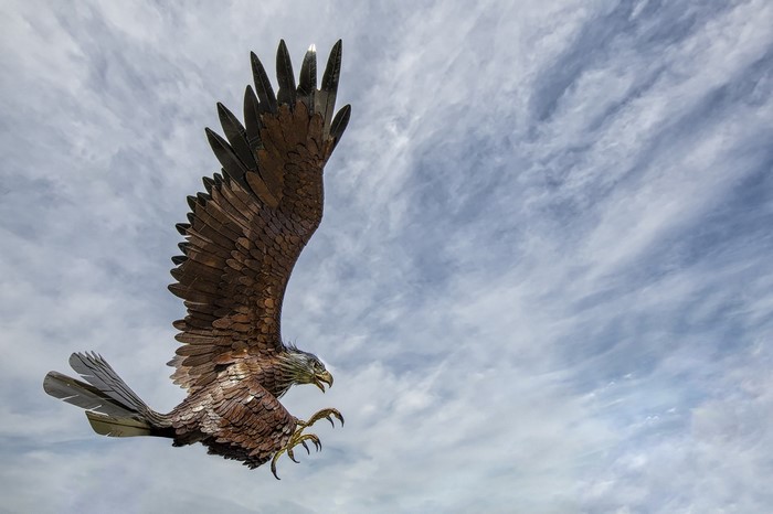 Metal eagle sculpture in flight against cloudy sky