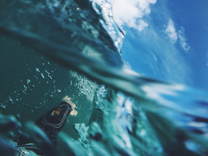 Underwater view of a surfer's leg with sky above