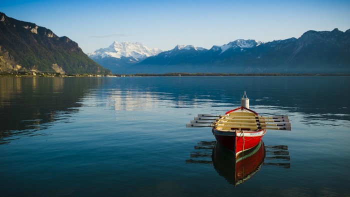 Red rowboat on a calm lake with mountains in the background