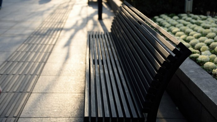 A dark slatted bench on a sidewalk with plants