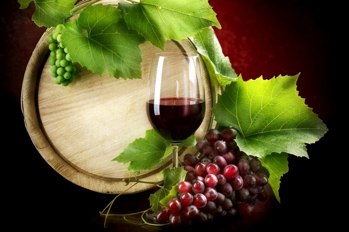 Red wine in a glass with grapes and a barrel