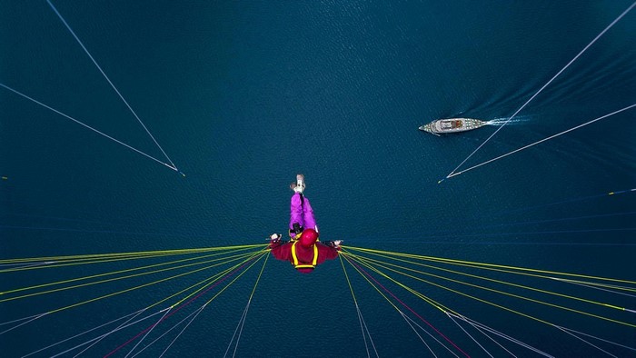 Paraglider over water with boat and lines