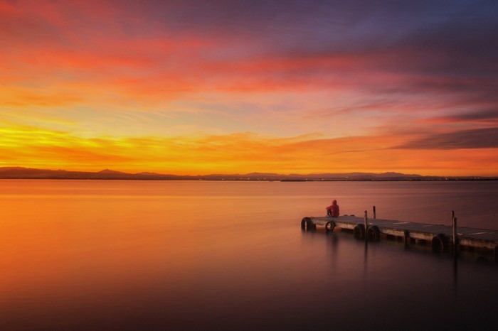 Person sitting on a dock at sunset over the water