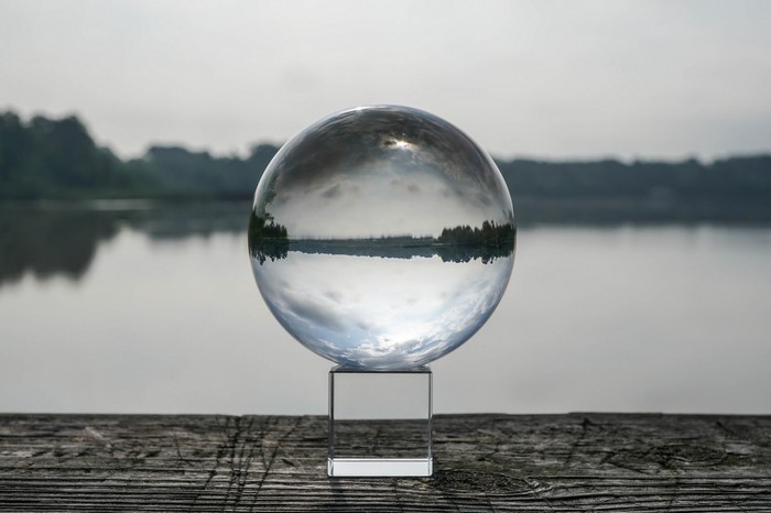 Glass sphere on wooden pier reflecting lake and trees