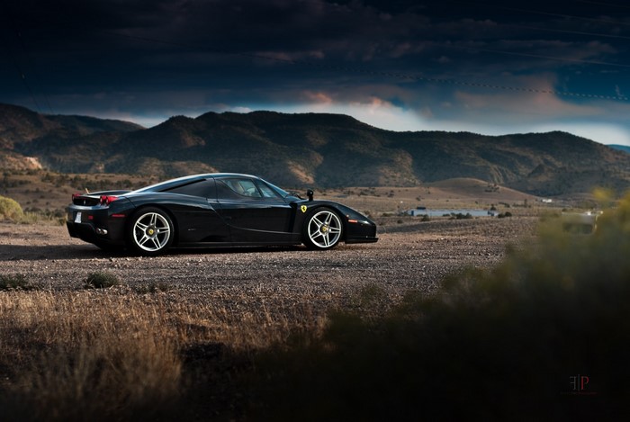 Black Ferrari Enzo parked on a dirt road with mountains