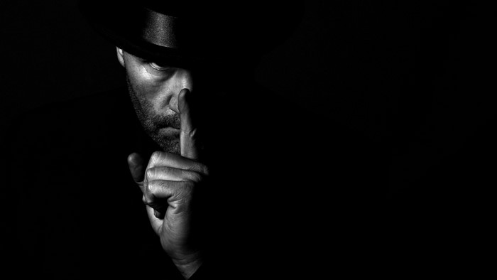 Man in hat making a shushing gesture in darkness