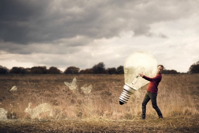 Man holding a giant lightbulb in a field