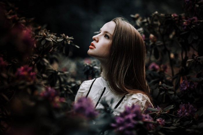 Woman in white dress surrounded by dark foliage and purple flowers