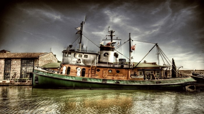 Vintage tugboat docked by a stone building