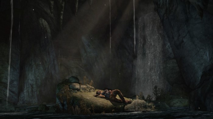 Lara Croft resting in a dark cave with waterfalls