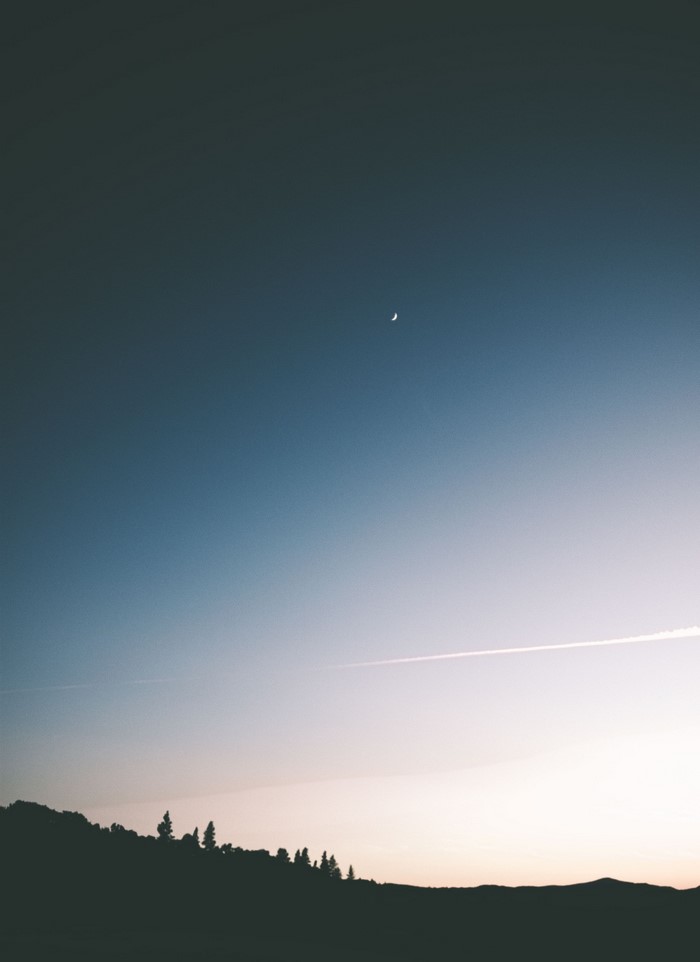 Crescent moon in the sky over silhouetted trees