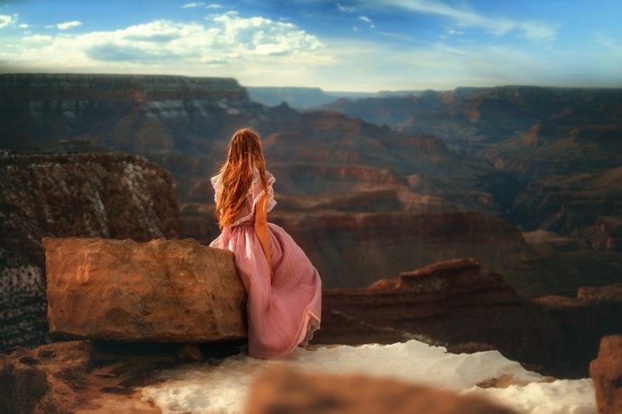 Woman in pink dress sitting on a rock overlooking the Grand Canyon