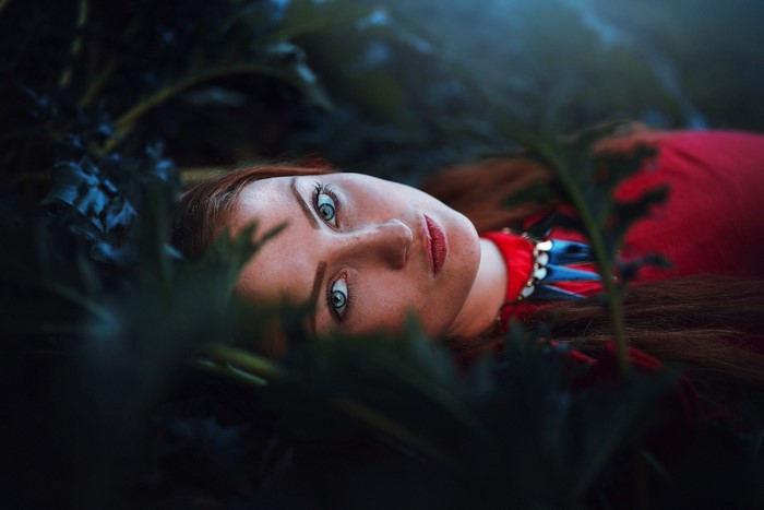 Woman with red hair lying among dark leaves
