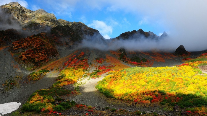 Mountain slope with autumn foliage and clouds