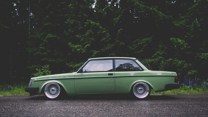 Green Volvo 240 Sedan parked by a forest