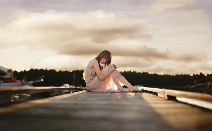 Woman in dress sitting on a dock at sunset