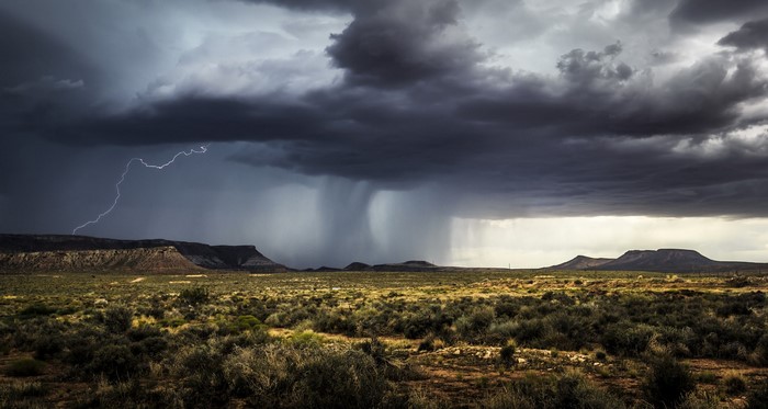 Lightning strikes over a stormy desert landscape with mesas
