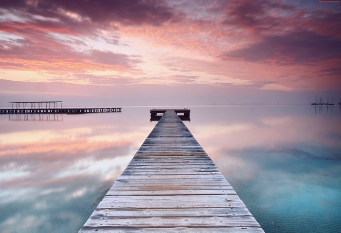 Wooden pier on calm water with pink clouds at sunset