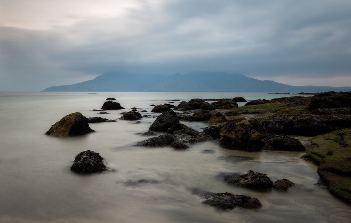 Rocky shore with mountains in the distance under cloudy sky