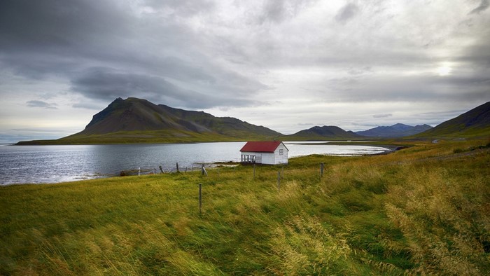 Small white house with red roof by a bay with mountains