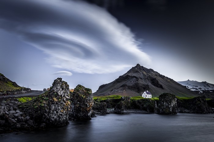 White house on a rocky coast with mountains and lenticular clouds