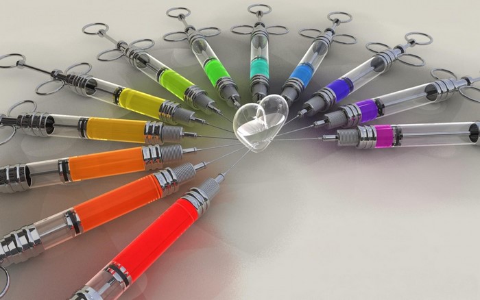 Syringes filled with colorful liquids forming a heart shape