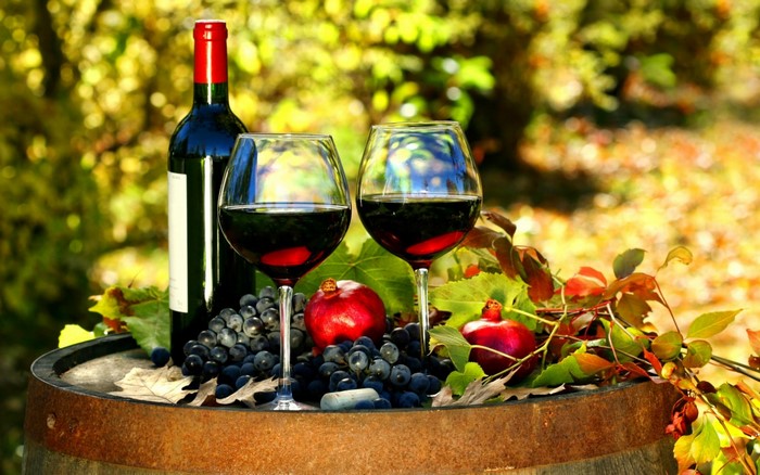 Wine bottle and glasses on a barrel with grapes and pomegranates