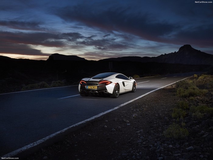 White McLaren 570GT driving on a road at dusk