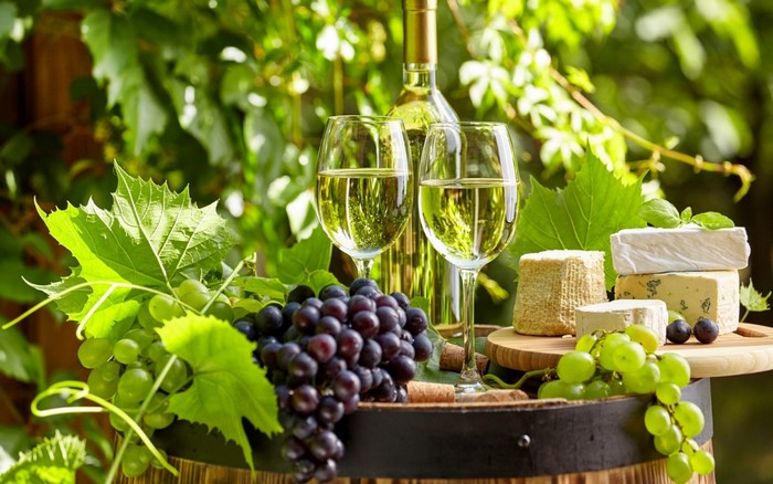 White wine with grapes and cheese on a barrel