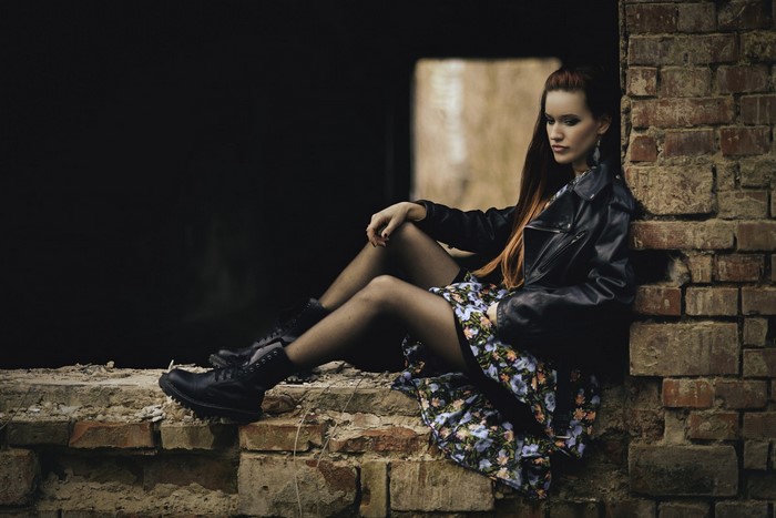 Woman in leather jacket and floral dress sitting on bricks