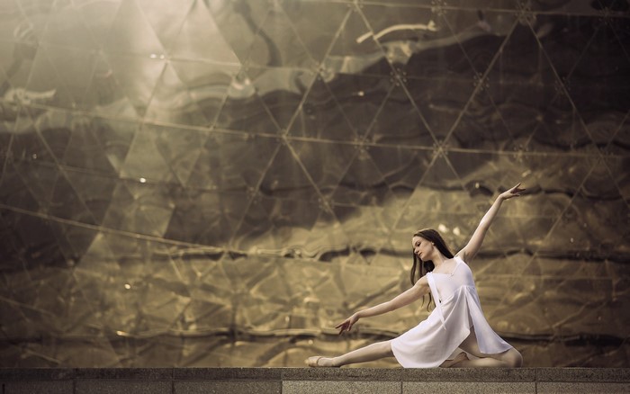 Ballerina in white dress posing against a geometric building