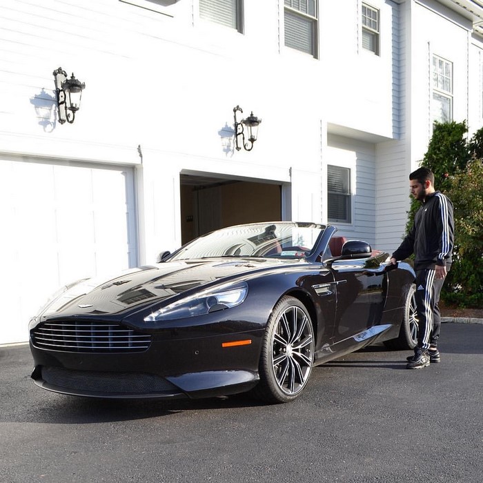 Man standing next to a black Aston Martin convertible in front of a white house