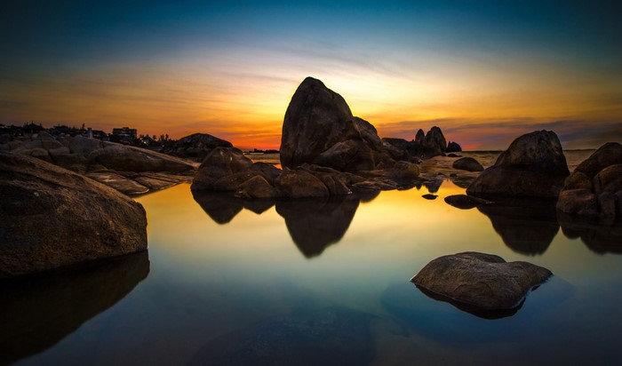 Sunset over rocky coast with calm sea reflection