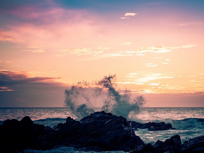 Wave crashing on rocks at sunset over the ocean