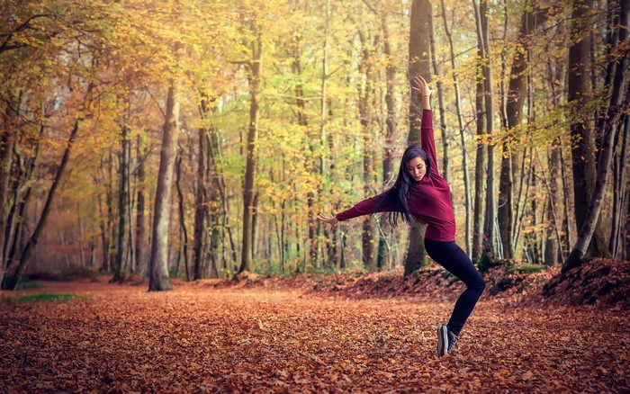 Woman dancing in an autumn forest with fallen leaves