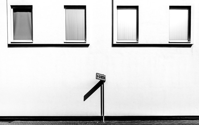 Monochrome image of a building facade with windows and a signpost